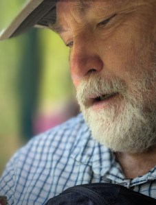 Man with grey beard looking down at unseen butterfly on his hand 